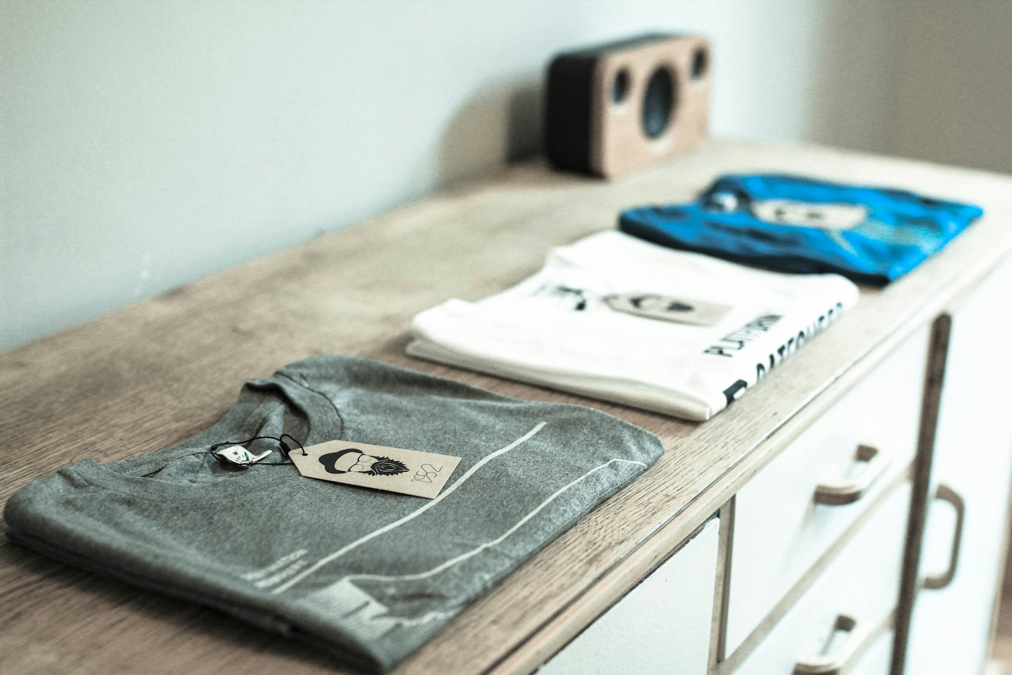 Grey, white, and blue folded t-shirts rest on a dresser.