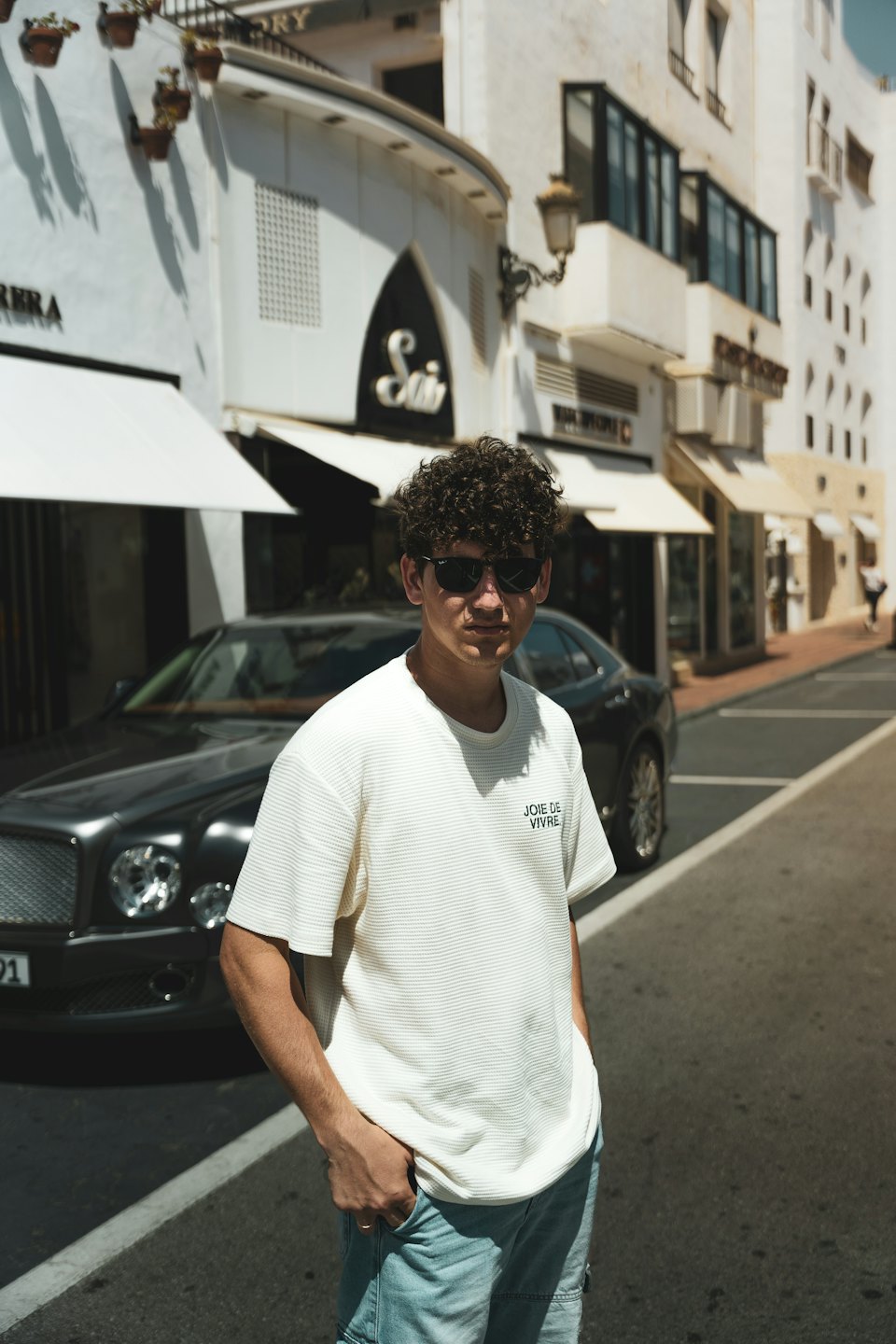 Man with sunglasses and hands in pockets on city street.