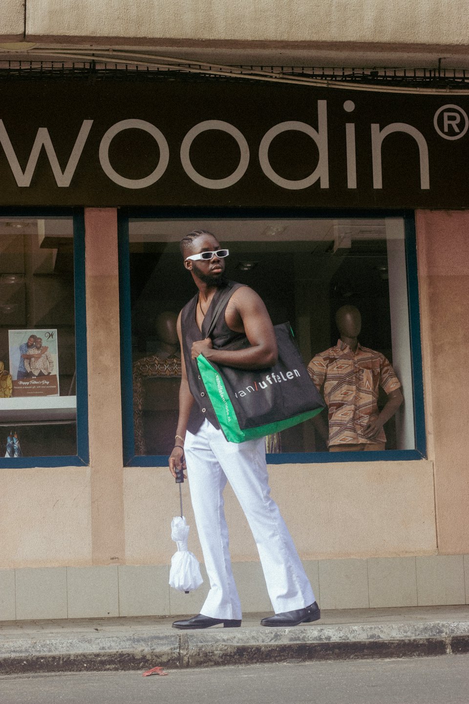 Man in white trousers walks on a city sidewalk.